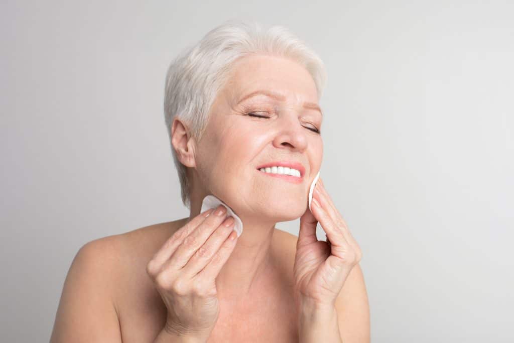 Elderly lady cleaning face with cotton pad