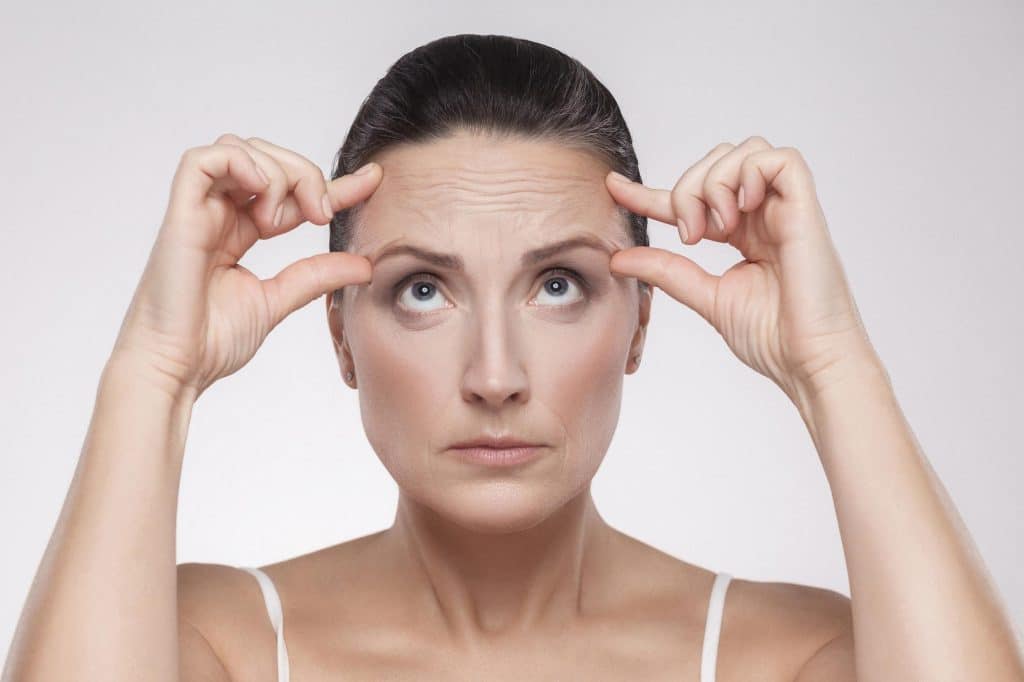 A middle-aged woman checks her forehead for wrinkles.